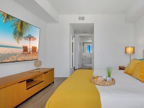 Een hotelkamer met een bed, een televisie, een houten dressoir en uitzicht op een strand.