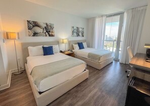 A hotel room with two beds, a desk, and a view of the city. - Breathtaking Bay View · 2BR · Beachwalk (Hallandale Beach)