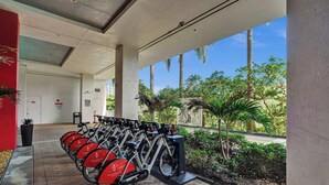 Un espacio al aire libre cubierto con una fila de bicicletas estáticas, un sendero y vistas a palmeras y follaje.