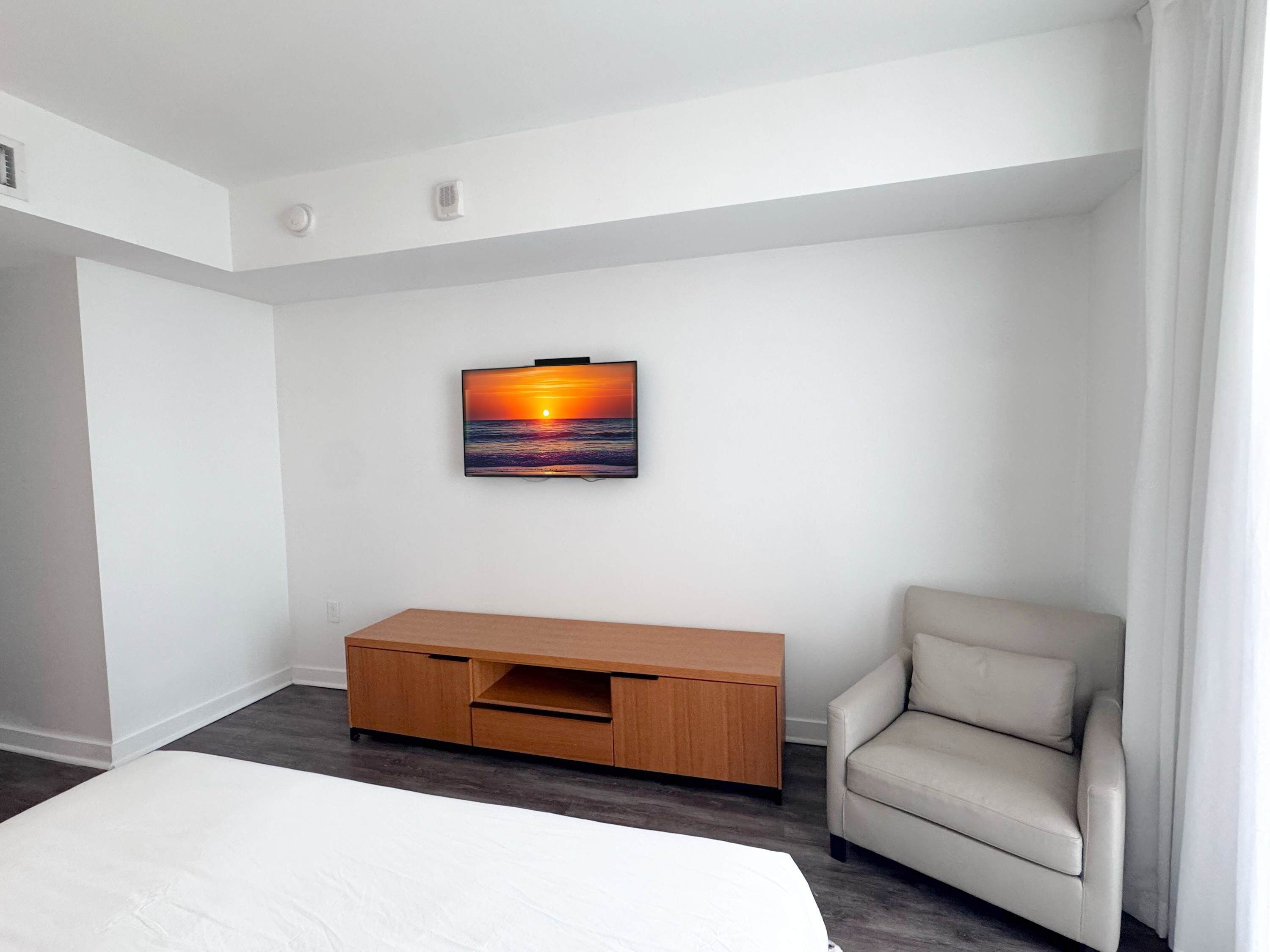 Habitación de hotel con cama, televisor montado en la pared, mueble de madera y una silla.