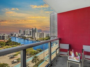 Un balcon avec un mur rouge, donnant sur une vue panoramique de la ville et d’une rivière.