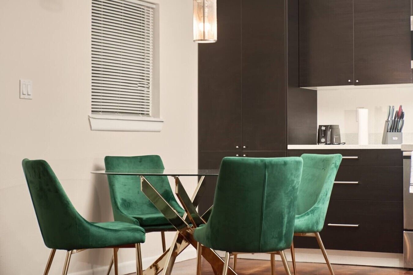 A modern kitchen with dark cabinets, a glass dining table, and green upholstered chairs.