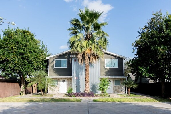 A two-story house with a central garage door, a palm tree in front, and a clear blue sky. - Near Airport  & Hospital / Fast WiFi / Parking (McAllen)