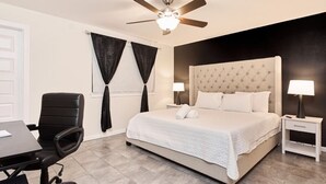 Une chambre à coucher comprenant un lit, un bureau, une chaise, un ventilateur de plafond et une table de chevet avec une lampe.
