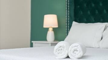 Un lit bien fait, avec du linge de lit blanc, une table de chevet blanche avec une lampe, et un mur d’accent vert.