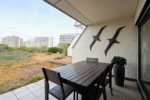 A patio with a table and chairs, a potted plant, and a wall-mounted bird sculpture. - Westduin GV003 + G19* (De Panne)