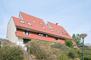 A multi-story building with a sloped roof, multiple windows, and a staircase leading to the entrance. - Westduin GV003 + G19* (De Panne)