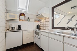 A modern kitchen with white cabinetry, a built-in microwave, a coffee maker, a stove, and a large window with a view of the sky. - Westduin GV003 + G19* (De Panne)
