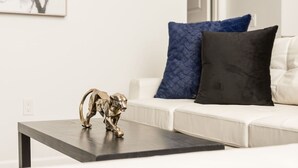 Een woonkamer met een witte bank, een donkere salontafel en een gouden beeldsje van een hond.