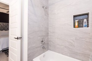 A bathroom with a bathtub, shower, and a small shelf with toiletries.
