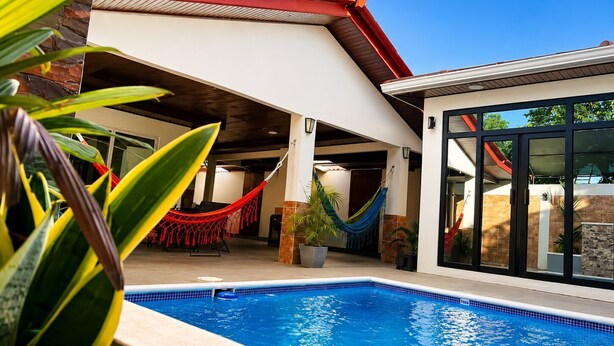 Una piscina con un área de techo rojo, una hamaca y plantas en macetas.