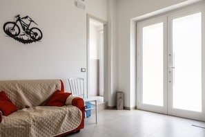 Un saló modern amb un sofà, una obra d'art amb una bicicleta penjada a la paret i una porta corredissa de vidre que fa a un espai exterior.