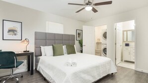 A bedroom with a bed, a desk, a chair, a ceiling fan, and a washing machine in the adjacent room. - Lux, First Floor, Fast-WiFi King Size (McAllen)