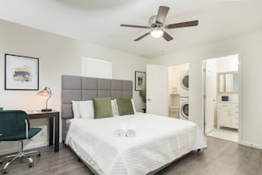 Ein Schlafzimmer mit Bett, Schreibtisch, Stuhl, Deckenventilator und einer Waschmaschine im angrenzenden Raum.