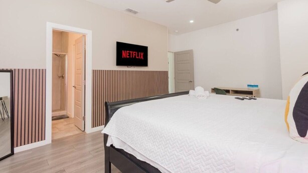 A hotel room with a bed, a TV mounted on the wall, a ceiling fan, and a shower area. - King Size Beds/ Fast WiFi / Spacious/ Close to DHR (Edinburg)