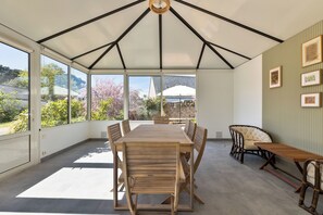 Eine überdachte Terrasse mit Holztisch und -stühlen, großen Fenstern und gerahmten Bildern an der Wand.