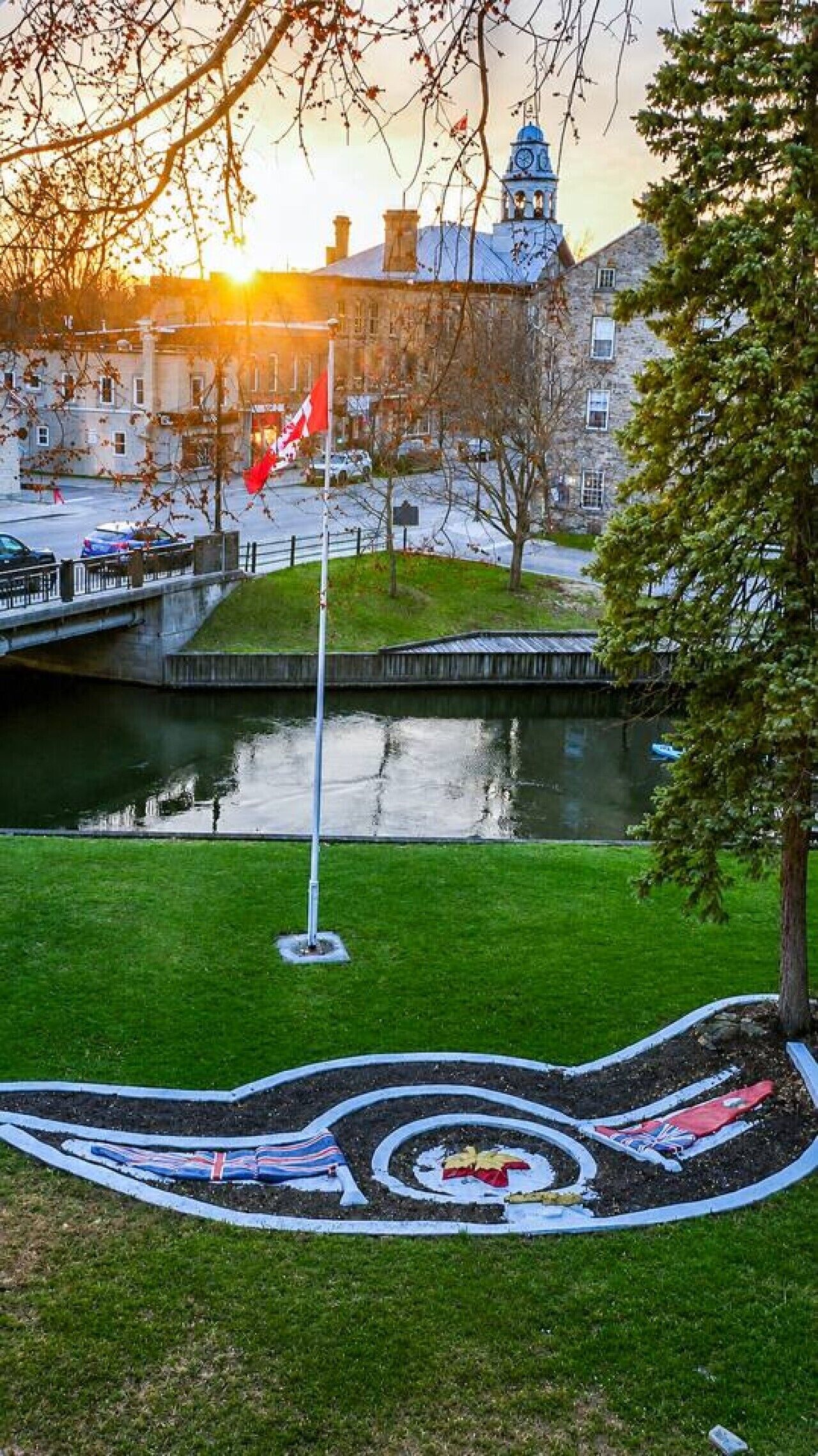 Uitzicht op een rivier met een vlag, een klokkentoren en een grasveld.