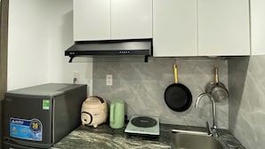 Een kleine keuken met een koelkast, een rijstkoker, een weegschaal en een spoelbak.
