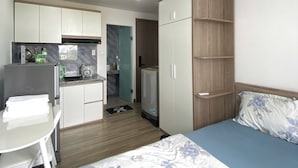 Een kleine kamer met een bed, een kitchenette, een tafeltje en een kledingkast.