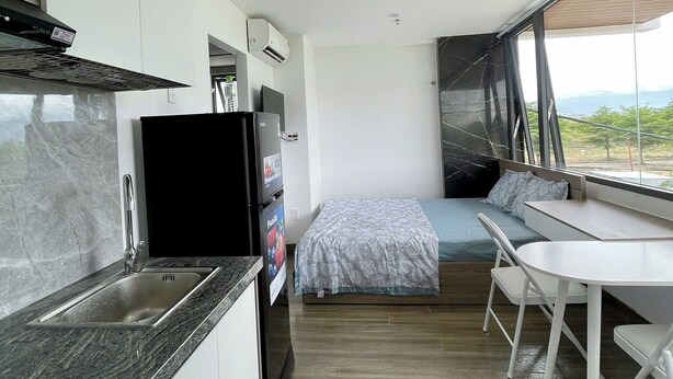 Een moderne keuken met een ingebouwde kookplaat, een spoelbak en een koelkast. Er is een zithoek met een tafel en stoelen, en een bed met uitzicht op de omgeving.