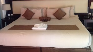Una cama bien hecha con almohadas y una toalla doblada, un cabecero de madera y mesitas de noche con lámparas.