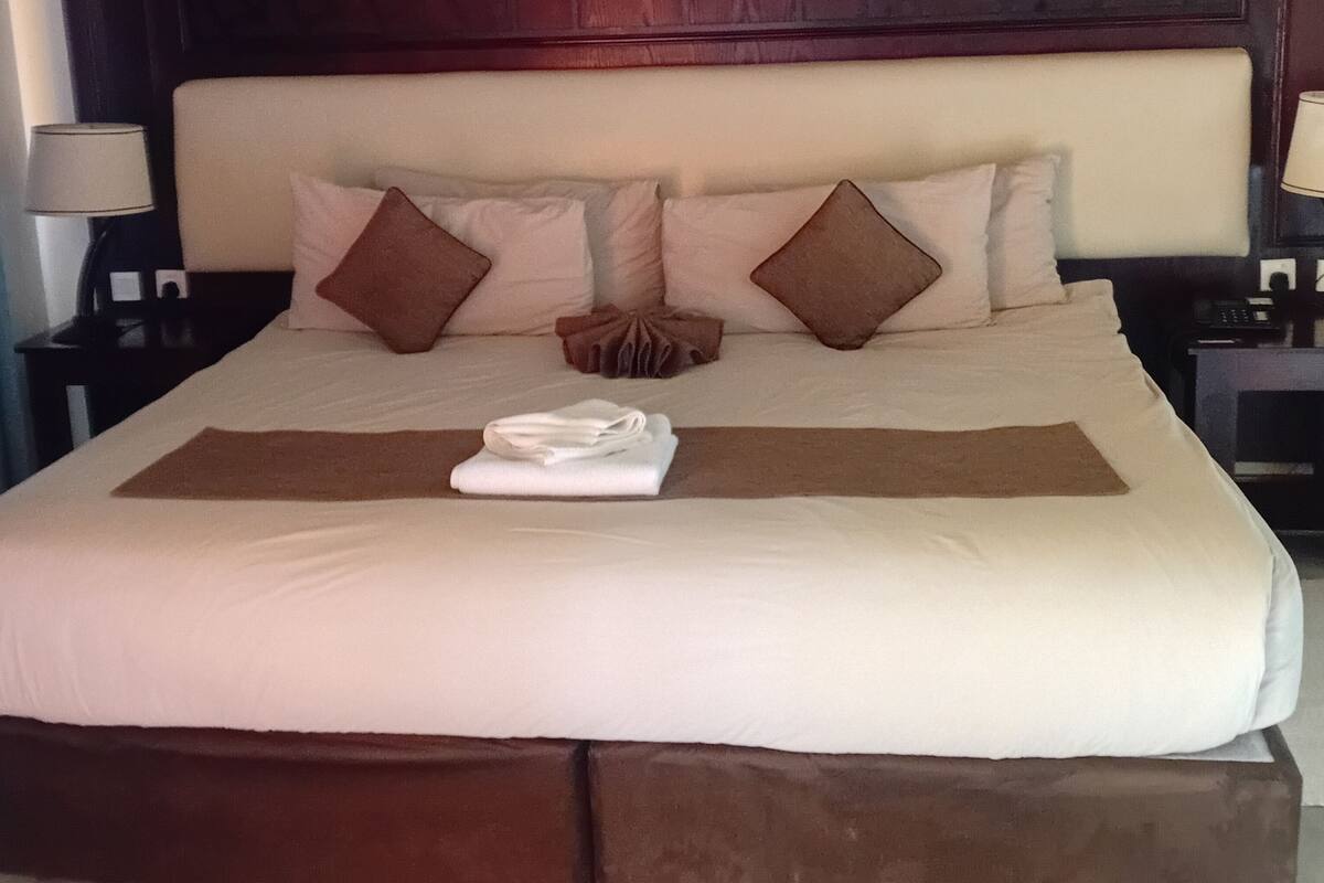Un lit bien fait, avec des oreillers et une serviette pliée, une tête de lit en bois et des tables de chevet avec des lampes.