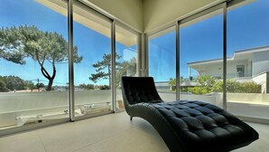 A modern room with a black lounge chair, large floor-to-ceiling windows, and a view of a residential area. - ROYAN PONTAILLAC UPSCALE VILLA "LES PINS" 2/4/6 PERSONS WITH POOL (Royan)