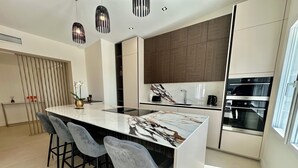 A modern kitchen with a marble island, bar stools, a built-in oven, and pendant lighting. - ROYAN PONTAILLAC UPSCALE VILLA "LES PINS" 2/4/6 PERSONS WITH POOL (Royan)
