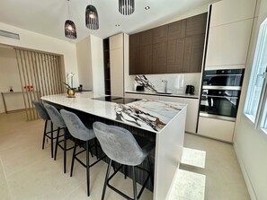 A modern kitchen with a marble island, bar stools, a built-in oven, and pendant lighting. - ROYAN PONTAILLAC UPSCALE VILLA "LES PINS" 2/4/6 PERSONS WITH POOL (Royan)