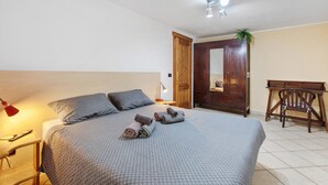 Een slaapkamer met een bed, nachtkastje, lamp, houten bureau en een deur.