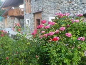 Un bâtiment en pierre doté d’un balcon et d’un jardin où poussent des fleurs roses.