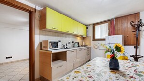 Een keuken met gele kastjes, een magnetron, een fornuis en een tafel met een tafelkleed met bloemen.