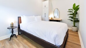 Un dormitorio con cama, mesita de noche, lámpara, armario, espejo y planta en maceta.