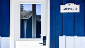 Una puerta blanca con un ventanal, una pared exterior azul, un letrero que dice 'THE ABERLOUR' y un felpudo con la palabra 'Nest'.