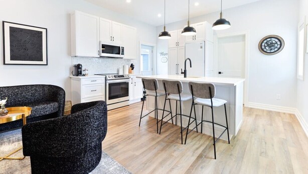 Una cocina moderna con armarios blancos, una isla central con taburetes y electrodomésticos como microondas y estufa.