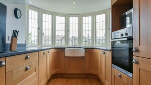 Una cucina con mobili in legno, un forno nero, un lavello e una finestra con vista sugli edifici.