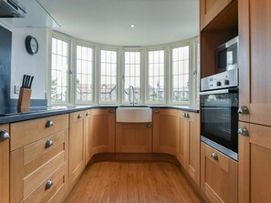 A kitchen with wooden cabinets, a black oven, a sink, and a window with a view of buildings. - Northrawe (Bamburgh)