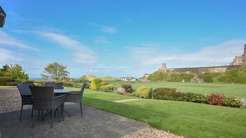 An outdoor patio with a table and chairs, a well-manicured lawn, and a castle in the background.