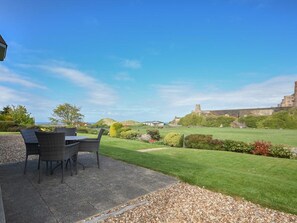 Eine Terrasse im Freien mit Tisch und Stühlen, ein gepflegter Rasen und eine Burg im Hintergrund.