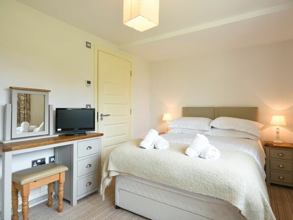 A hotel room with a bed, bedside lamps, a television, a mirror, a desk with a chair, and a door. - Northrawe (Bamburgh)