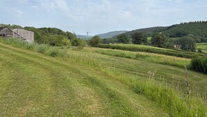 Ländliche Landschaft mit einem baufälligen Bauernhof, sanften Hügeln und blauem Himmel.