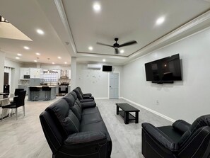 A modern living room with a black leather sofa, a TV mounted on the wall, and a ceiling fan.