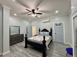 A bedroom with a bed, dresser, mirror, ceiling fan, and an air conditioning unit.