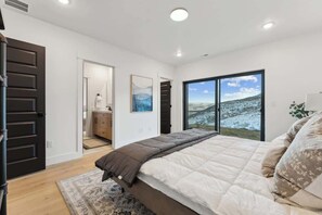 Une chambre à coucher avec un lit, une grande fenêtre donnant sur la montagne, une porte et une petite salle de bain.