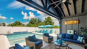 Ein Poolbereich mit Korbmöbeln, einem blauen Sofa und einem Deckenventilator.