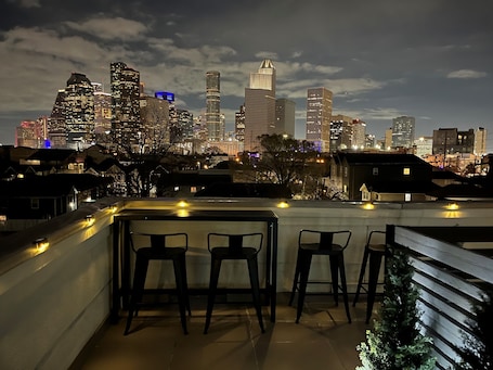 A rooftop terrace with bar stools and a view of a city skyline at night.. Modern Houston House / Rooftop Terrace / Downtown Skyline Views / 3BR 3.5BA