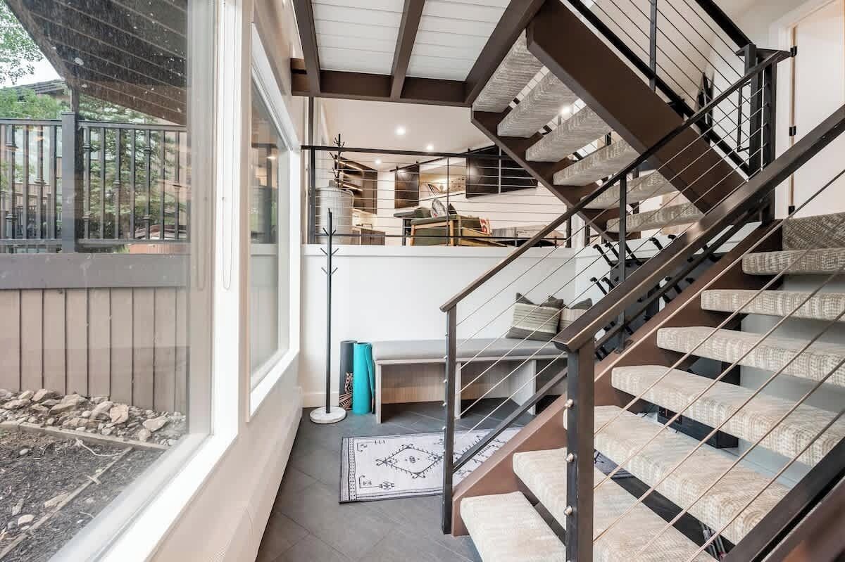 Un escalier moderne avec une rampe en métal, une vue sur une pièce comprenant un canapé et une table basse, et une fenêtre donnant sur un jardin.