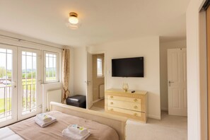 Ein Schlafzimmer mit Bett, Kommode, Fernseher und Balkon.