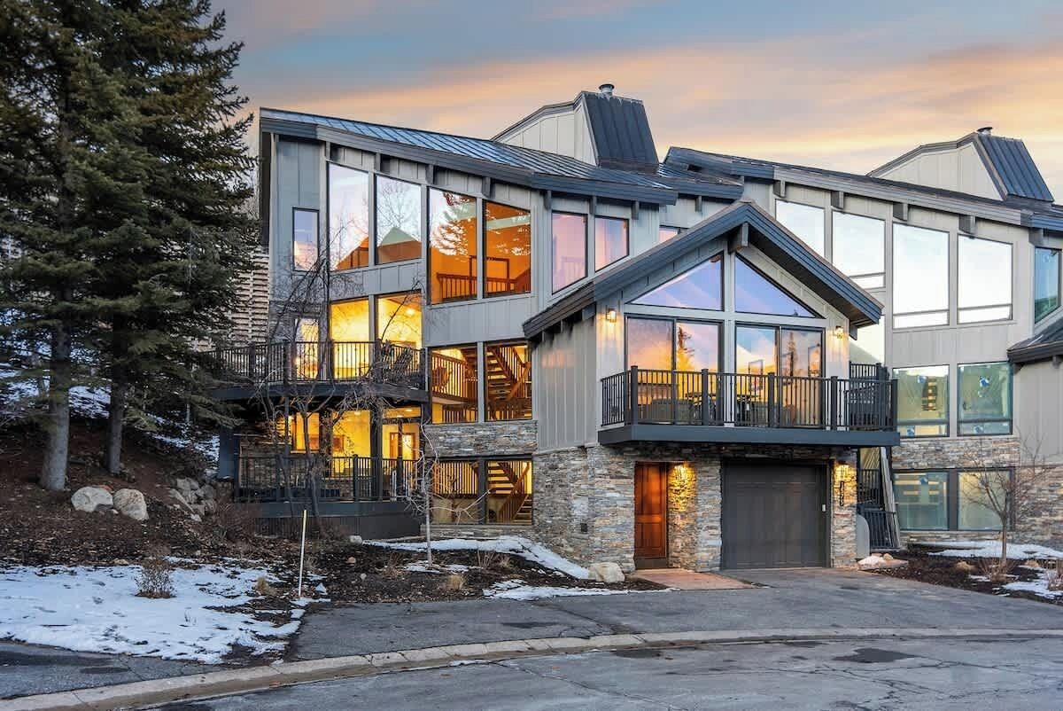 A modern multi-story house with large windows, a stone facade, and a balcony.