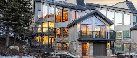 A modern multi-story house with large windows, a stone facade, and a balcony.